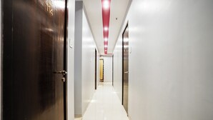 A corridor with doors on both sides, a tiled floor, and a red ceiling light. - Hotel Elegance (Mumbai)