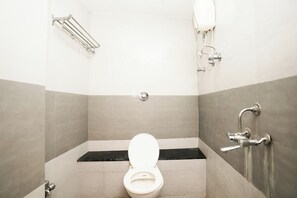 A small, tiled bathroom with a white toilet, a metal towel rack, and a wall-mounted faucet. - Hotel Elegance (Mumbai)