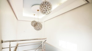 A staircase with a metal handrail, a white wall, and a ceiling with a geometric light fixture. - Hotel Elegance (Mumbai)