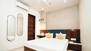 A bedroom with a bed, two bedside tables, a wardrobe, a mirror, and an air conditioning unit. - Hotel Elegance (Mumbai)
