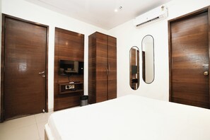 A bedroom with a bed, wooden wardrobe, a TV shelf, a mirror, and an air conditioning unit. - Hotel Elegance (Mumbai)