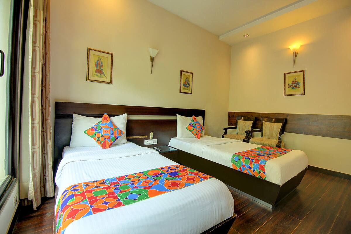 A hotel room with two beds, each with a colorful geometric-patterned bedspread, a wooden headboard, and a nightstand with a lamp.