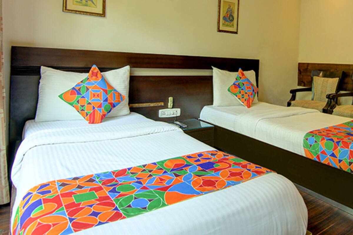 A hotel room with two beds, each with a colorful geometric-patterned bedspread and matching pillows.