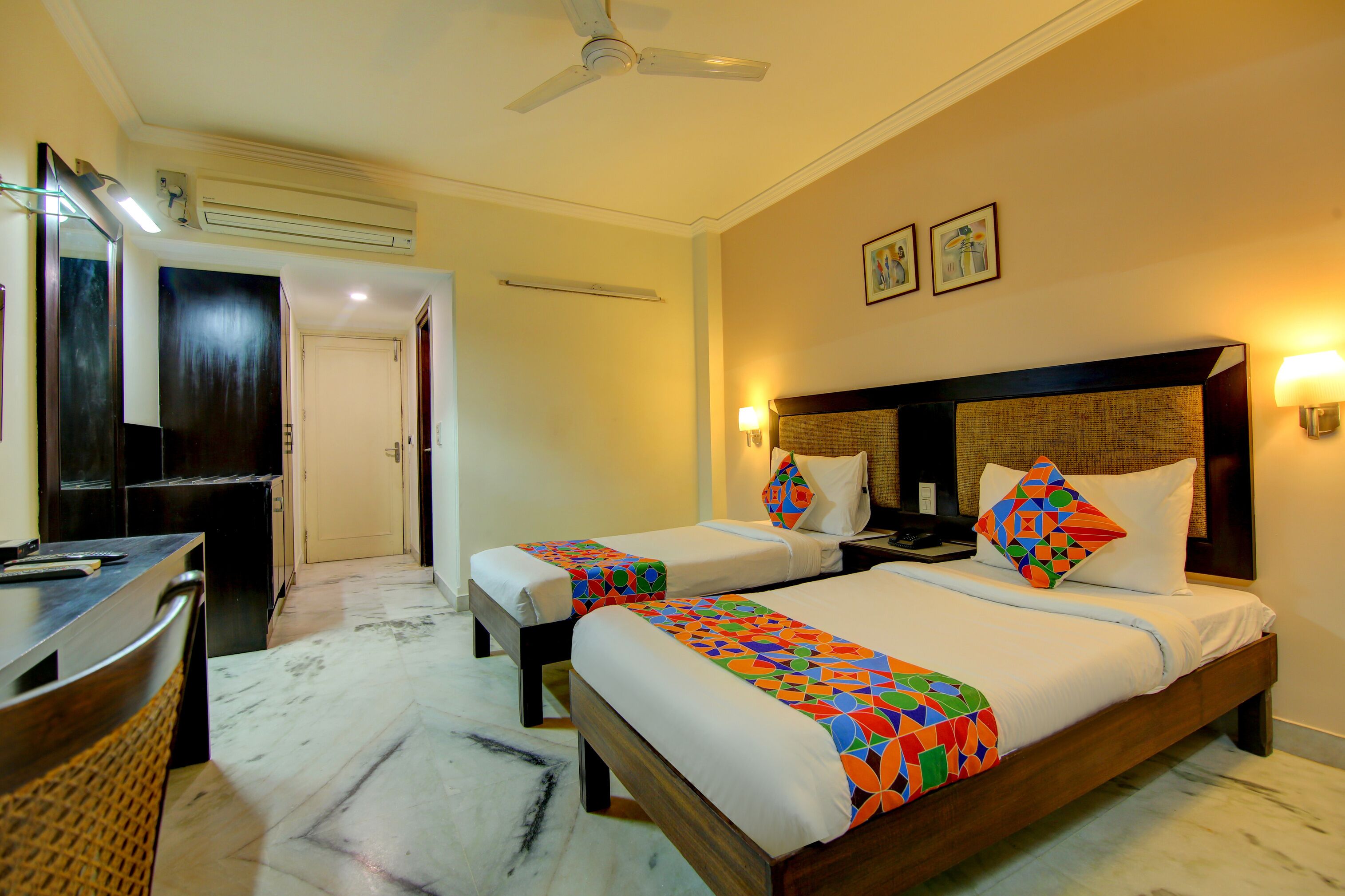 A hotel room with two beds, a desk, a chair, and a ceiling fan.
