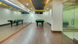 A billiards room with two billiard tables, a glass partition, and a ceiling with linear lighting. - Fabhotel Staywell (Gurugram)