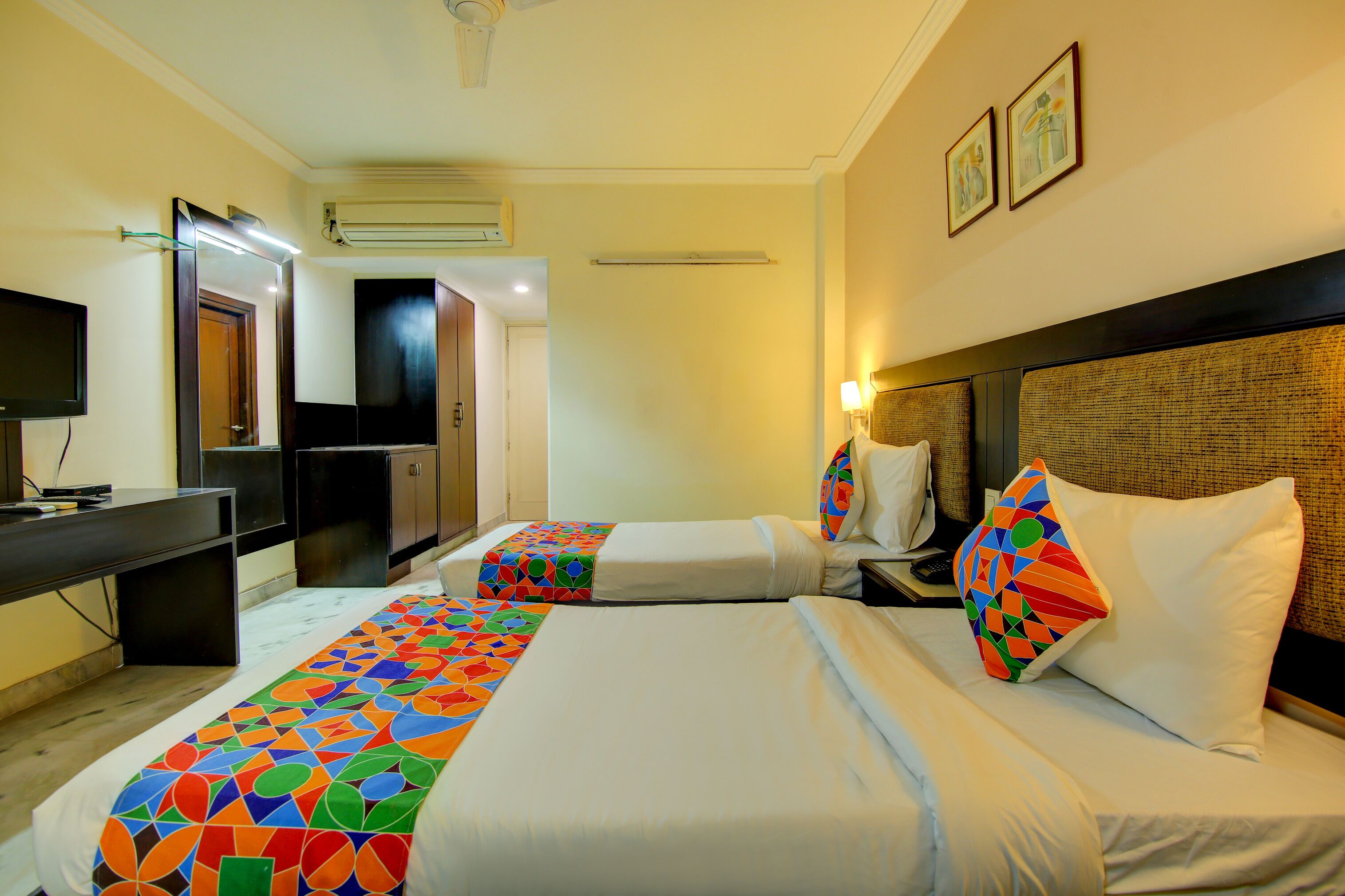A hotel room with two beds, a desk, a TV, and a bathroom visible through an open door.