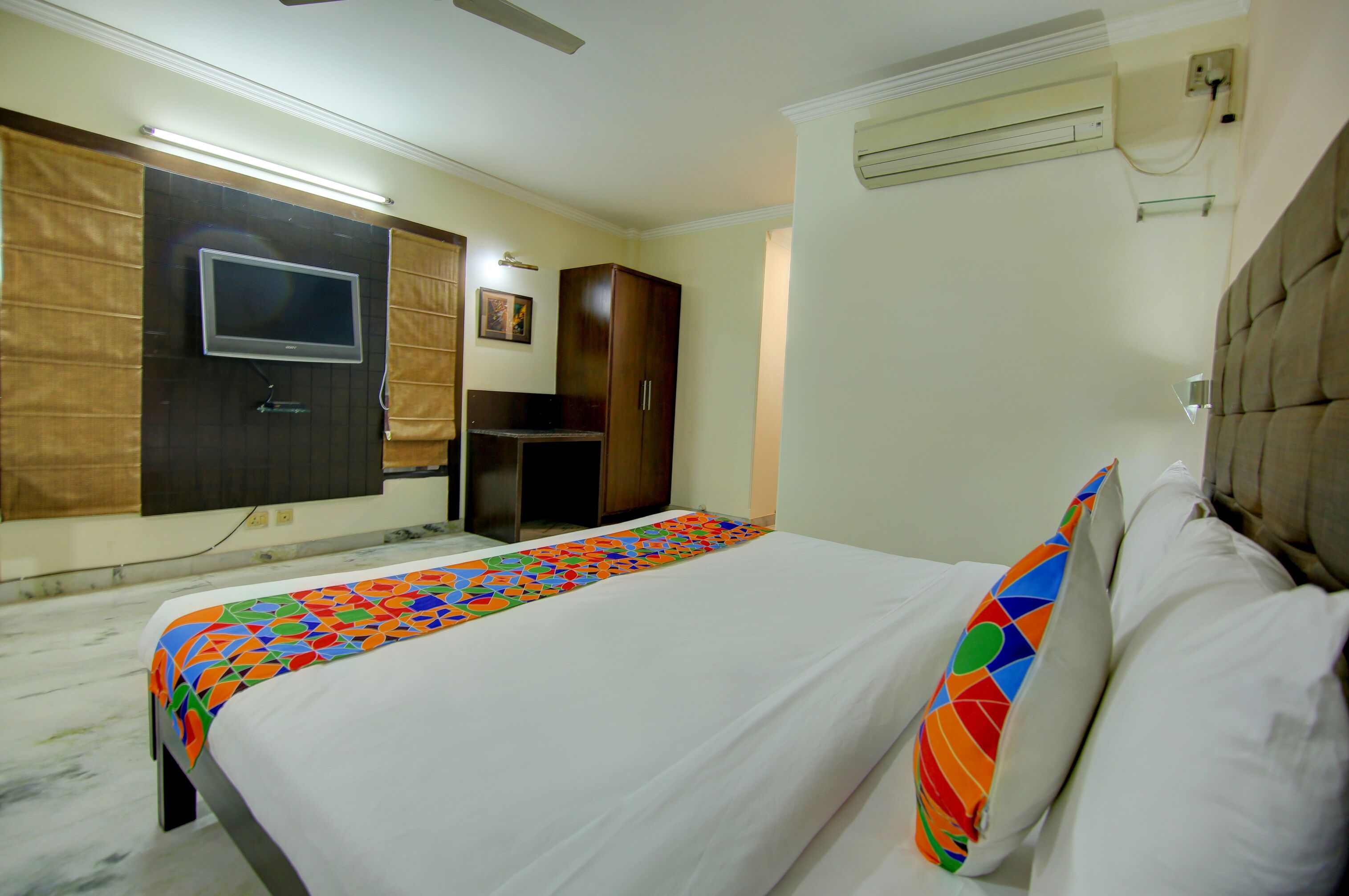 A hotel room with a bed, a TV mounted on the wall, a wardrobe, and a ceiling fan.