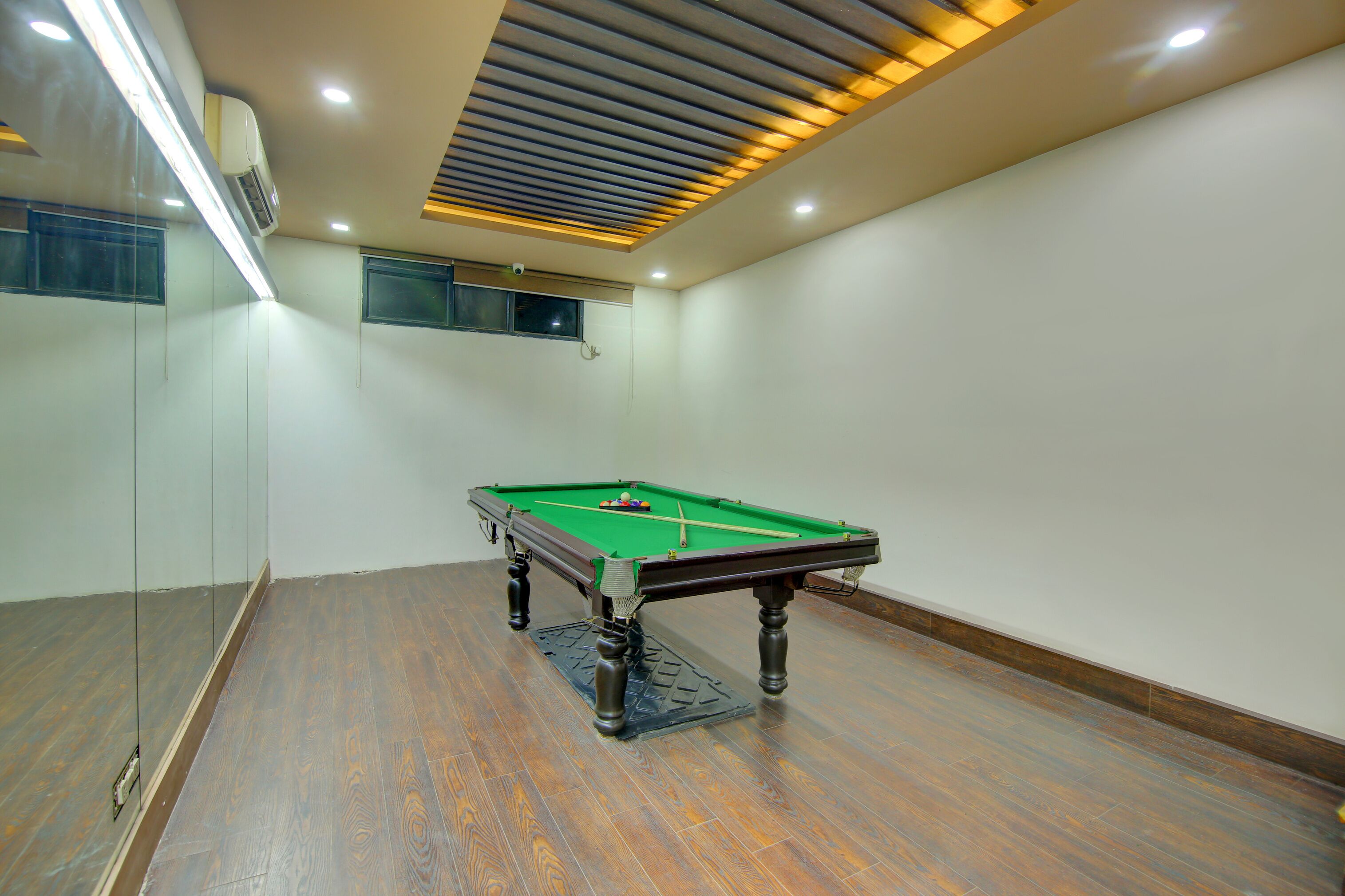 A pool table in a room with wooden flooring, a ceiling with recessed lighting, and a wall-mounted air conditioning unit.