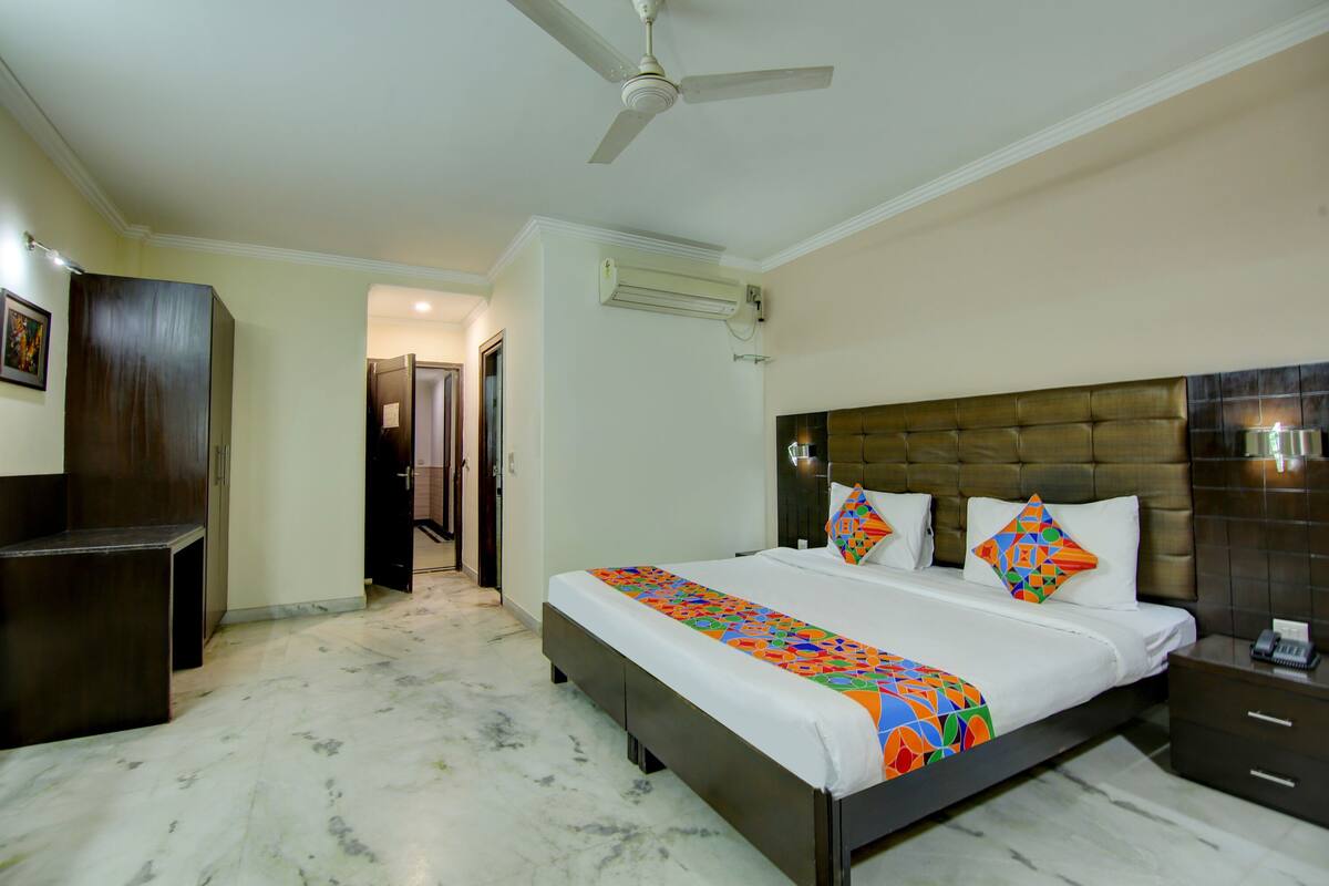 A hotel room with a bed, a nightstand, a desk, a ceiling fan, and an air conditioning unit.