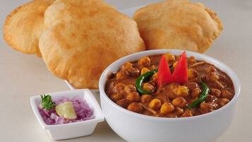A bowl of chickpea curry with a side of sliced onions and a small bowl of chutney, accompanied by three pieces of bread.