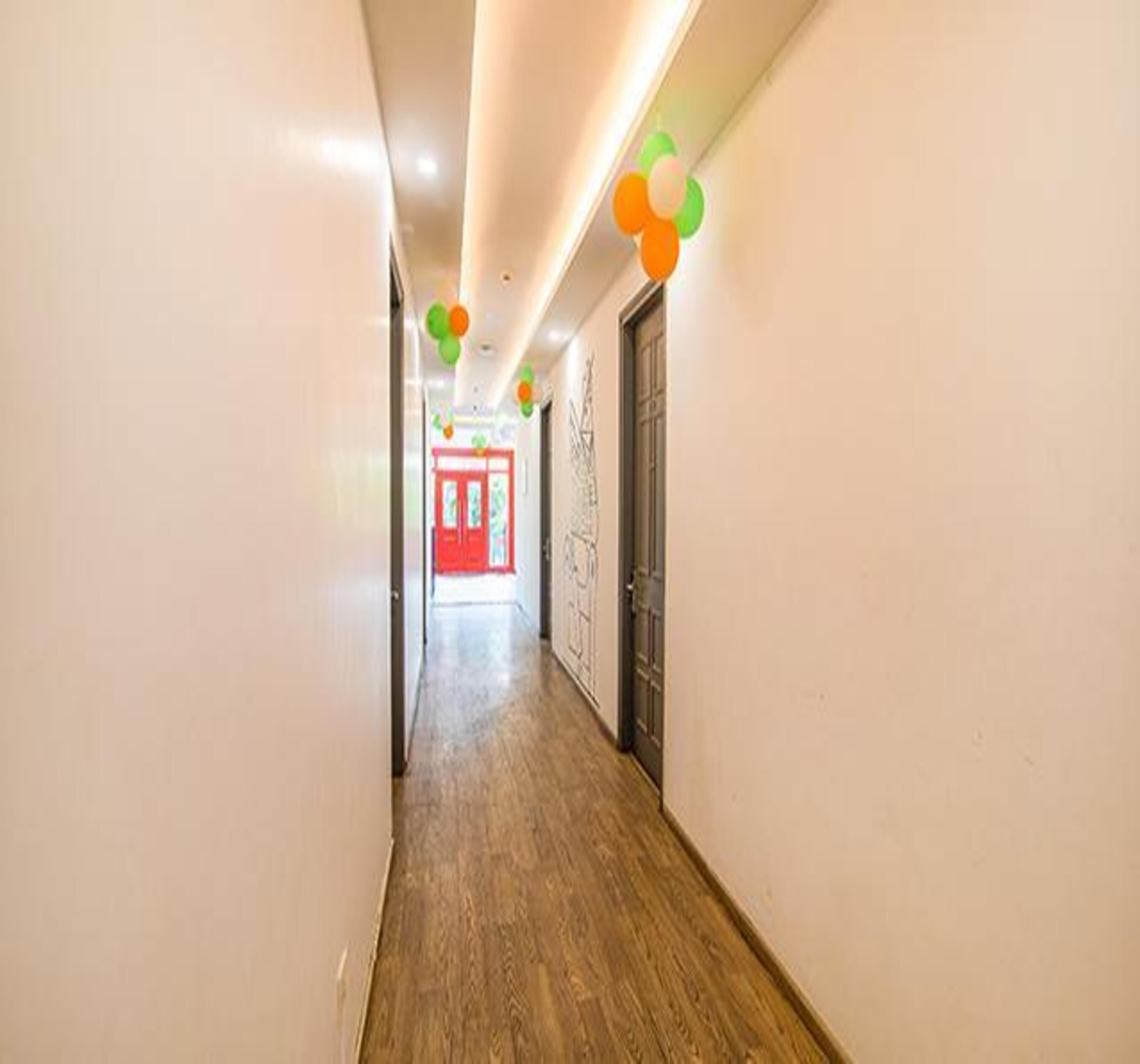A hallway with wooden flooring, white walls, and a red door at the end.