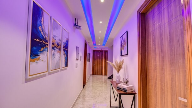 A hallway with framed artwork on the walls, a wooden door on the right, and a console table with decorative items. - FabHotel Gross inn Suites (New Delhi)