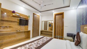 A modern bedroom with a large bed, wooden wardrobe, a ceiling fan, and a TV mounted on the wall. - FabHotel Gross inn Suites (New Delhi)
