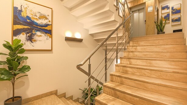 Una escalera con escalones de mármol y barandales de metal, una planta en maceta y un cuadro en la pared.
