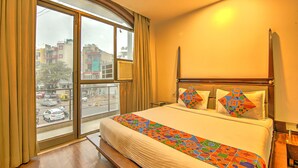 Una habitación de hotel con un ventanal grande, una cama con una colcha colorida y un cabecero de madera.