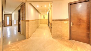 Un pasillo de hotel con suelo de mármol, puertas de madera y pared azulejada.