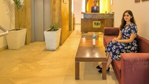 Zona de recepción de hotel con recepcionista, mostrador, una mesa de centro y asientos.