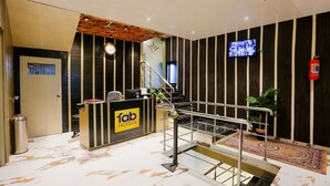 Zona de recepción de un hotel, con mostrador de recepción, un reloj, televisión y una escalera.