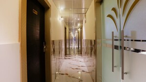 Un pasillo con piso de mármol, una puerta con la leyenda '101' y un separador de vidrio con un diseño metálico decorativo.