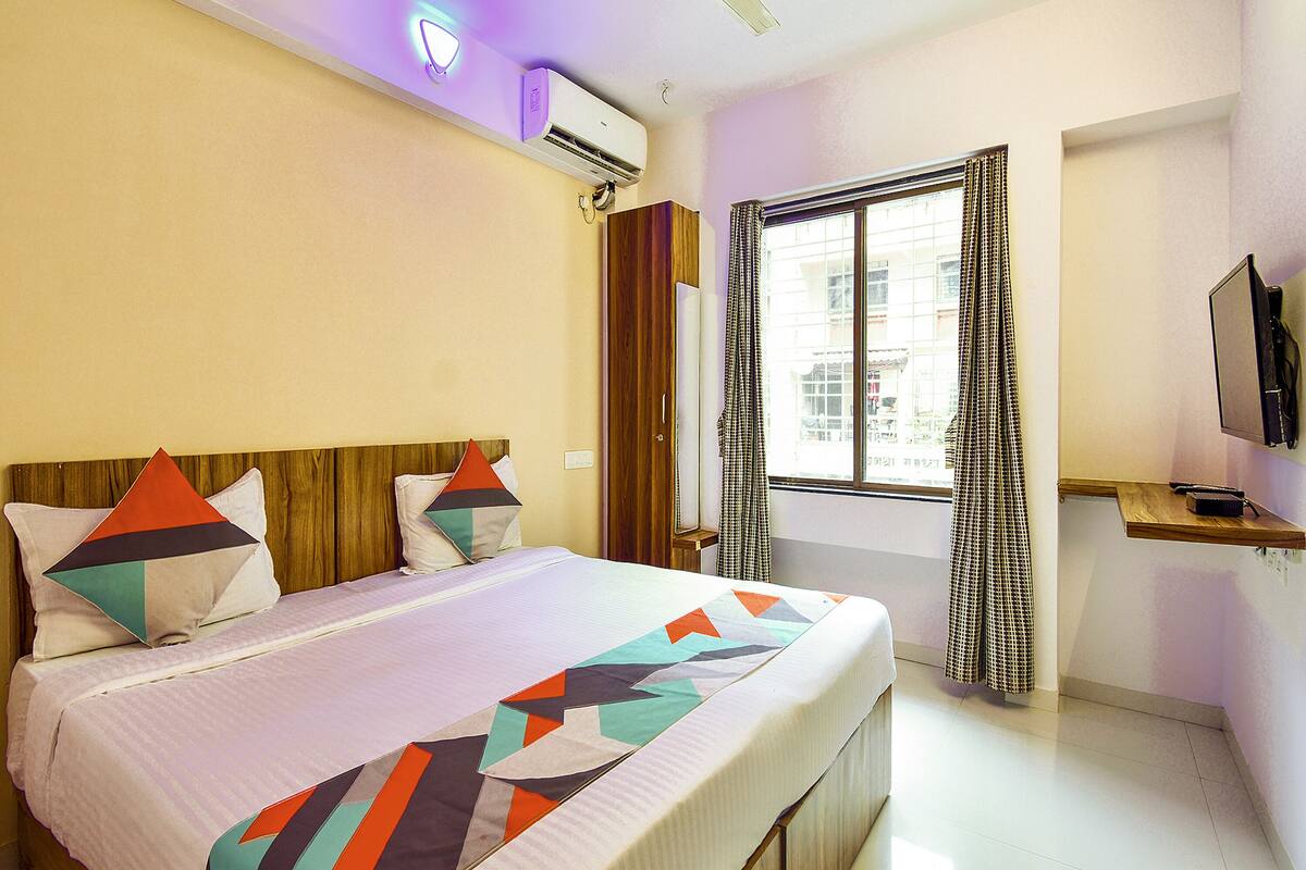 Quarto de hotel com cama, televisão e janela com cortinas.
