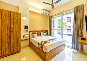 A modern bedroom with a wooden bed, a wardrobe, a bedside table, and a large window with curtains. - FabHotel Habitat (Pune)