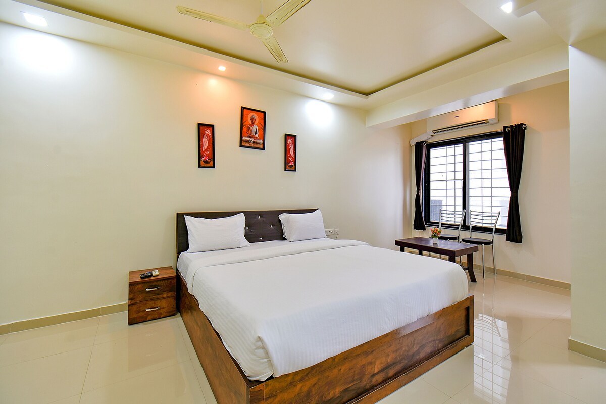 A hotel room with a large bed, a bedside table, a chair, a ceiling fan, and a window with curtains.