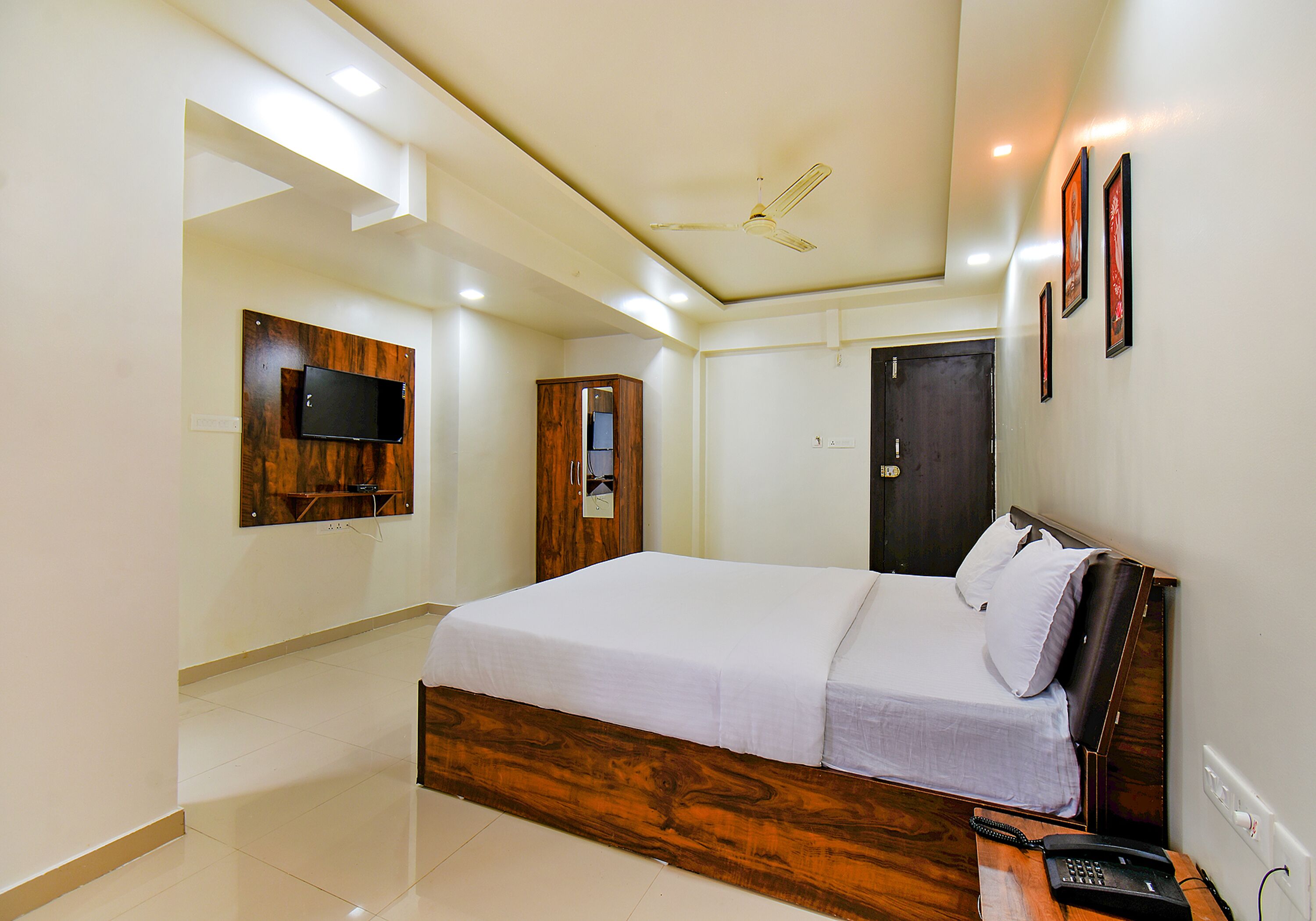 A bedroom with a wooden bed frame, a flat-screen TV mounted on the wall, a wardrobe, and a door.