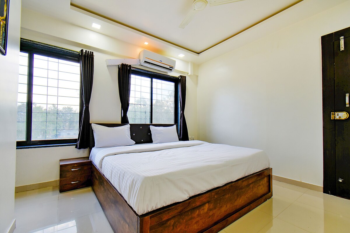 A bedroom with a wooden bed, a nightstand, a window with curtains, and an air conditioning unit.