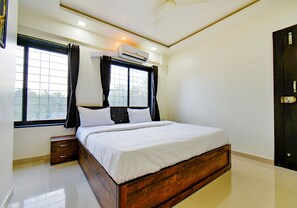 Een slaapkamer met een houten bed, een nachtkastje, een raam met gordijnen en een airconditioning.