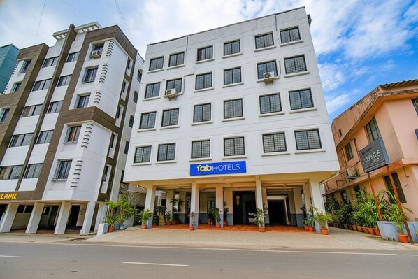 Een hotel met meerdere verdiepingen, een moderne gevel, een opvallend 'fabHOTELS'-bord en een overdekte entree met plantenpotten.