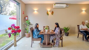 A dining area with a table, chairs, potted plants, and an air conditioning unit on the wall. - Fabhotel Grand Inn (Jalandhar)