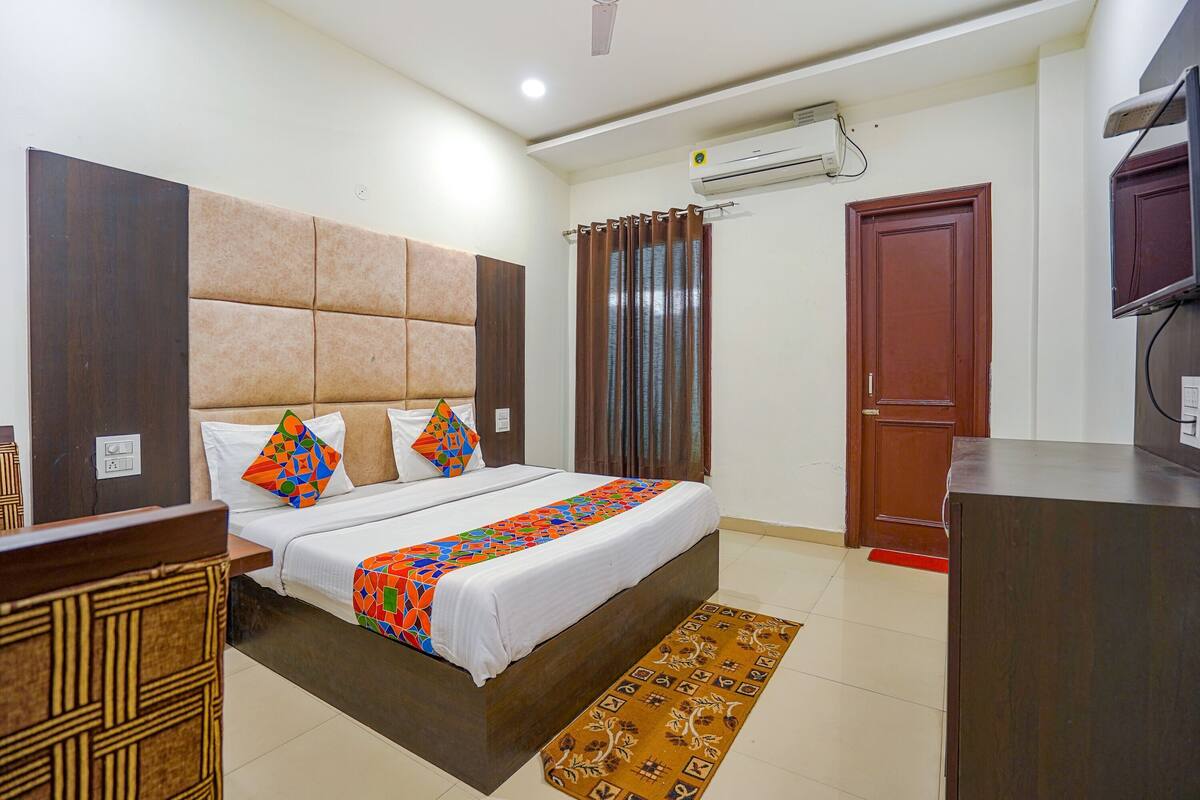 A hotel room with a bed, a desk, an air conditioner, a door, and a ceiling fan.