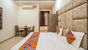 A hotel room with a bed, a small table, chairs, an air conditioning unit, and a view of the outside. - Fabhotel Grand Inn (Jalandhar)