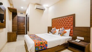 Una habitación de hotel con una cama, una mesita de noche de madera con un teléfono, un aire acondicionado instalado en la pared y una puerta que da a otra habitación.