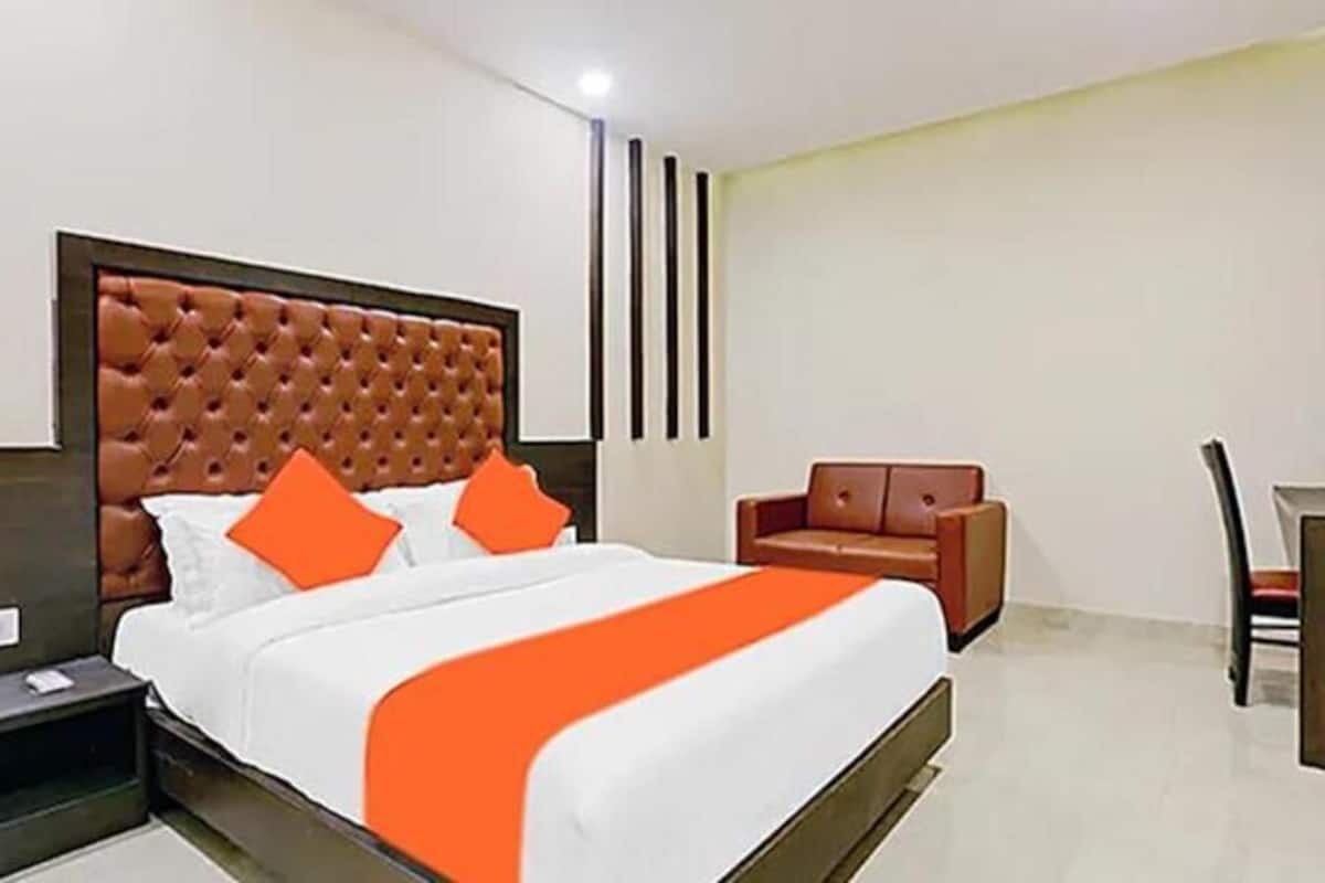 A hotel room with a large bed, a wooden headboard, a sofa, a desk, and a chair.