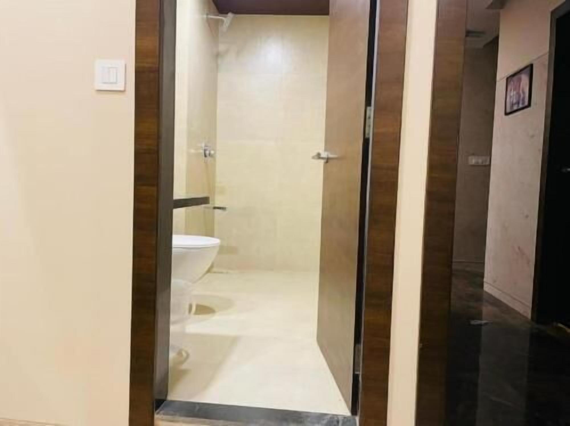 A narrow, tiled bathroom with a toilet and a shower.