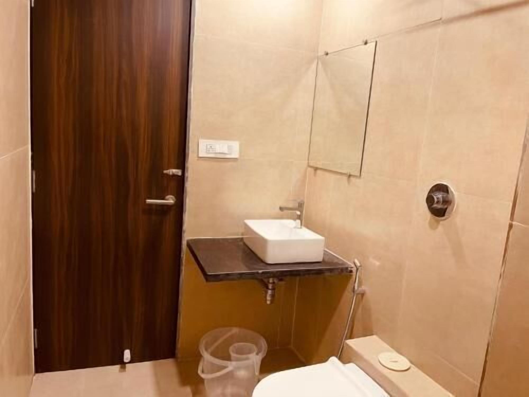 A small bathroom with a wooden door, a white sink, a mirror, and a toilet.