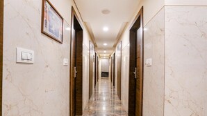 Un pasillo con suelo de mármol, con puertas a ambos lados, iluminación empotrada y un cuadro en la pared izquierda.