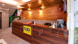 A reception desk with a wooden finish, a 'fob hotels' sign, and three pendant lights. - FabHotel Elite Peak (Noida)
