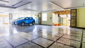A spacious lobby with a blue SUV parked in the center, a fire extinguisher mounted on the wall, and a potted plant near the entrance. - Fabhotel Surya Grand I (Vijayawada)