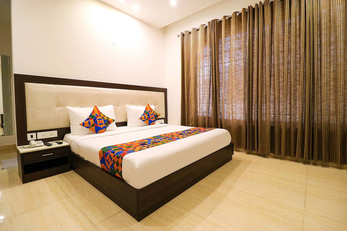 A hotel room with a large bed, a nightstand with a phone and remote, and a window with curtains.