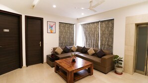 A living room with a sofa, a coffee table, and a ceiling fan. - FabHotel Oyster Villa - Nr. Paras Hospitals Sushant Lok 1 (Gurugram)