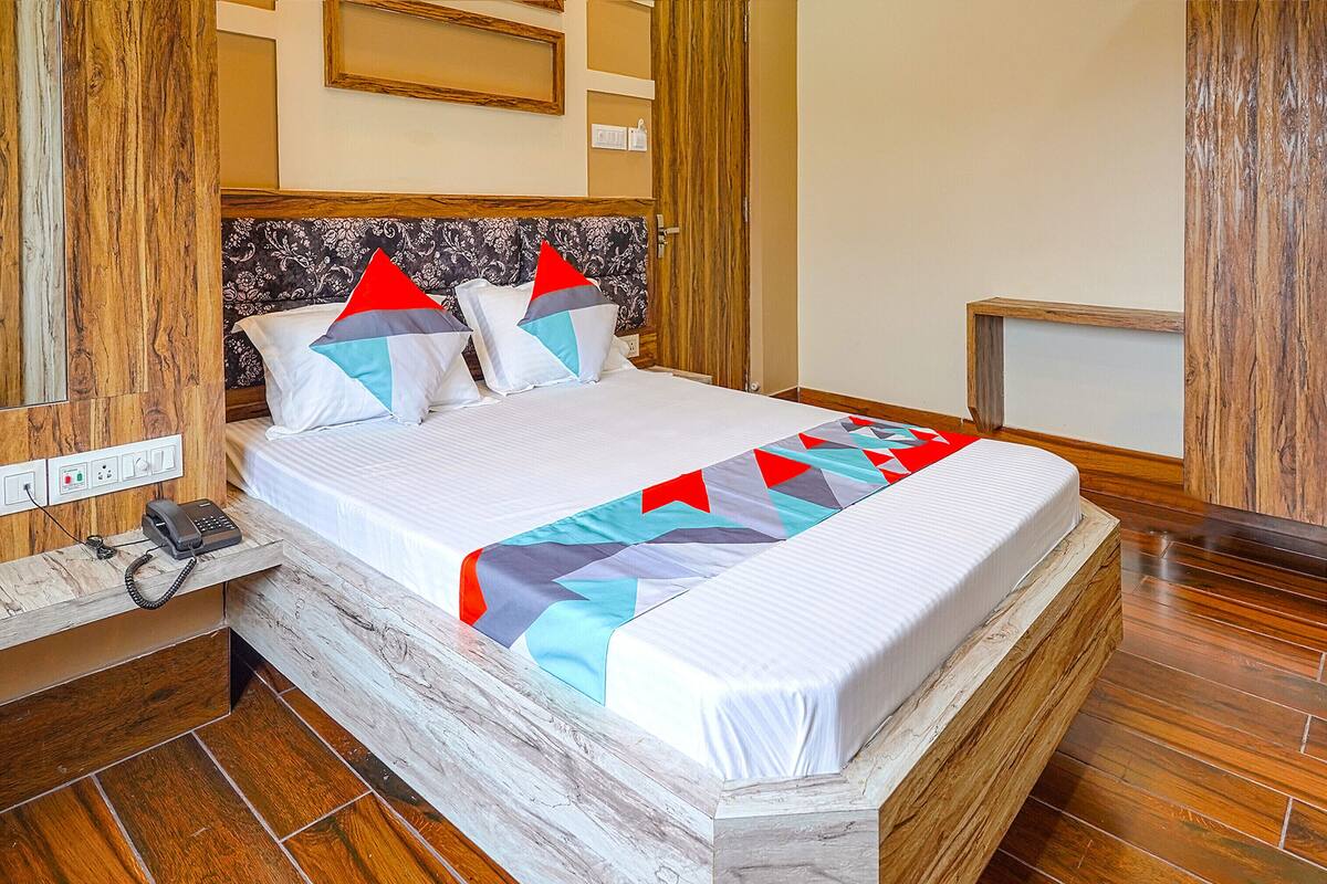 Una cama bien hecha con un cabecero estampado, un teléfono en la mesita de noche y una mesita de noche de madera.