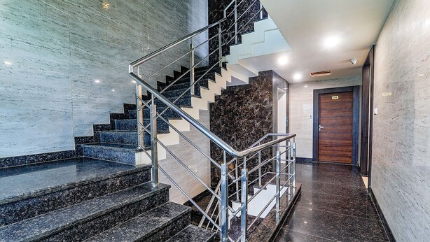 A modern staircase with metal railings, marble steps, and a polished floor leading to a wooden door.