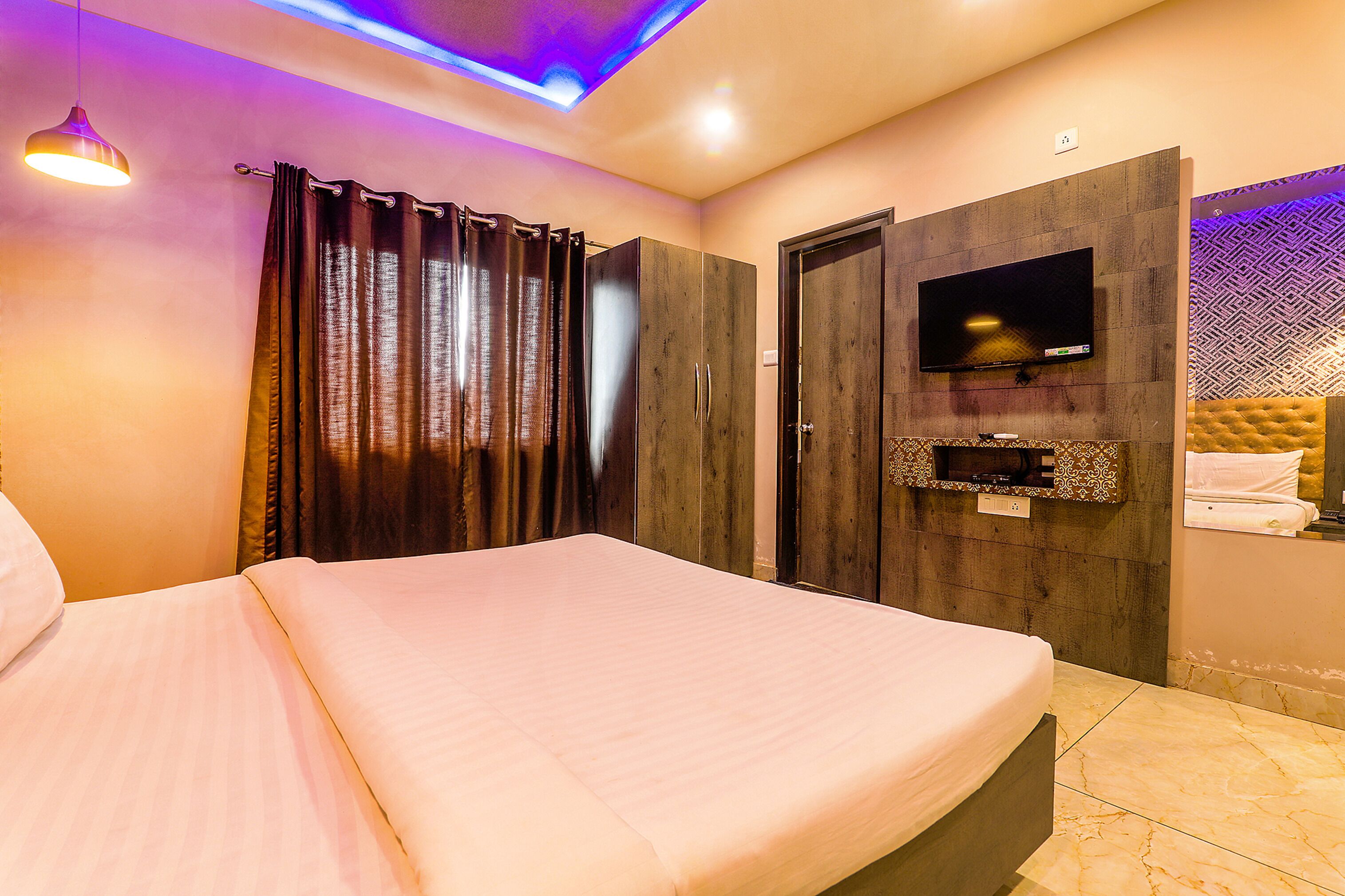 A bedroom with a bed, a TV mounted on the wall, and a ceiling light fixture.