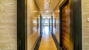 A hallway with a marble floor, wooden doors, and a decorative ceiling light fixture.
