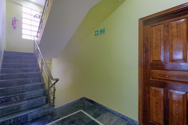 A staircase with a fire exit sign, a wooden door, and a window with blinds.