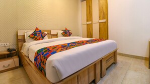 A neatly made bed with a colorful geometric-patterned blanket, a wooden headboard, and a bedside table with a lamp. - Fabhotel The Royal Oak (Gurugram)