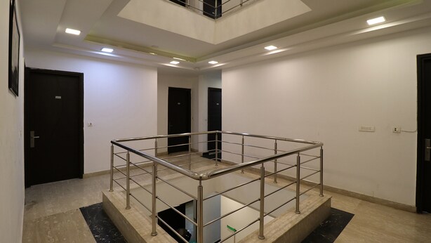 A spacious, modern interior with a central glass railing, multiple doors, and recessed lighting. - Fabhotel The Royal Oak (Gurugram)