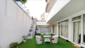 A courtyard with artificial grass, white wicker furniture, and potted plants. - Fabhotel The Royal Oak (Gurugram)